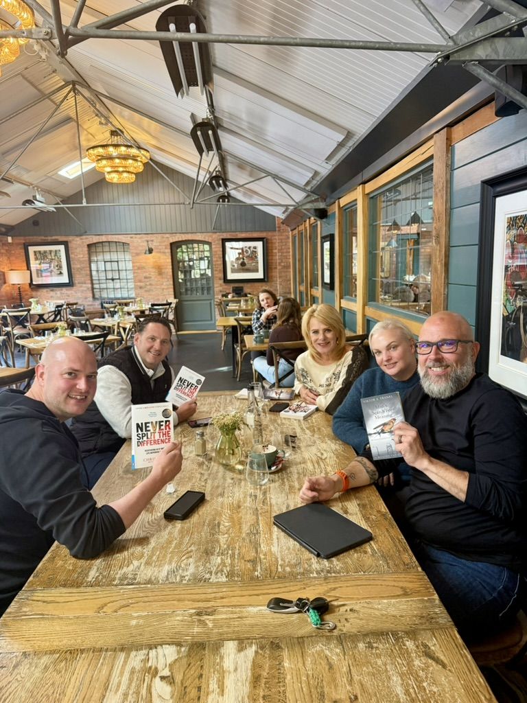Members around the table, holding copies of Never Split the Difference and Man's Search for Meaning